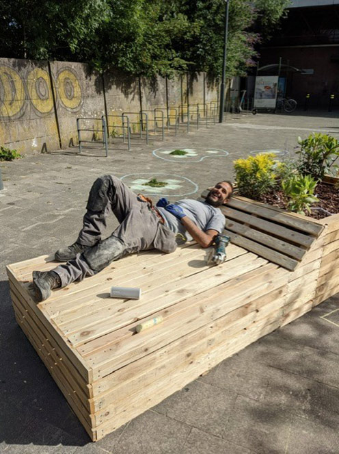 Un ouvrier couché sur un banc en bois qui contient un bac à fleurs